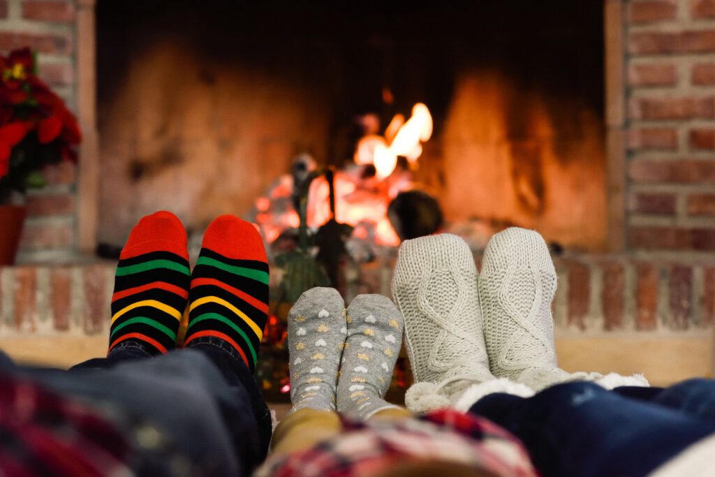 Eine Familie hat es sich an einem kalten Wintertag gemütlich gemacht. Alle tragen warme Socken und strecken ihre Füße Richtung Kamin, um sich zu wärmen.