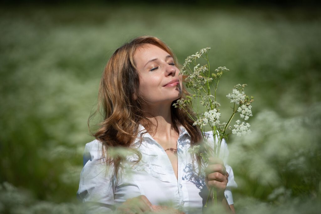 Eine Frau steht in einem blühenden Feld und genießt den Duft einiger gepflückter Blumen.