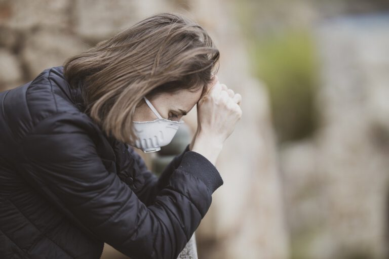 Eine Frau trägt eine Gesichtsmaske und schaut erschöpft und hilflos nach unten.