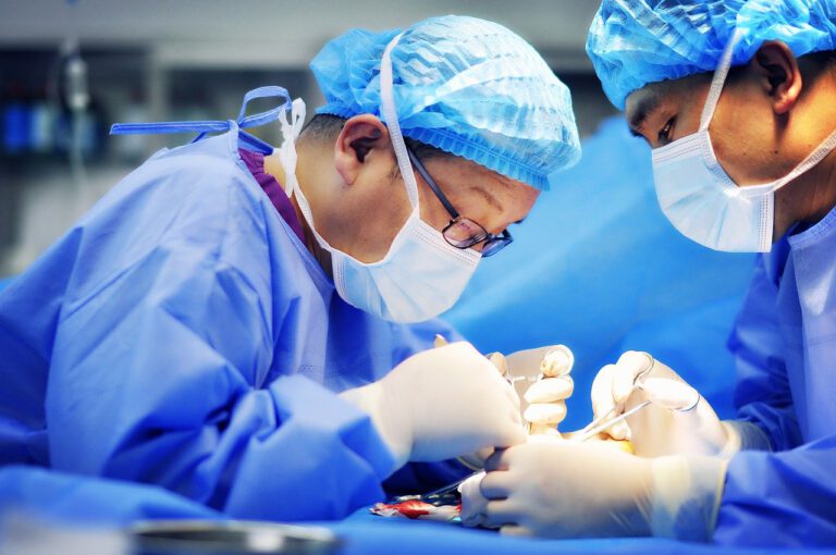 Zwei Chirurgen in blauer OP-Kleidung führen eine Operation durch.
