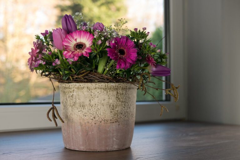 Auf einer Fensterbank steht ein dekorativer Blumentopf mit einem Gesteck aus frischen lila Blumen.