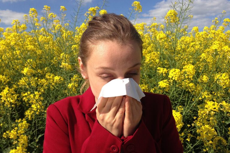 Eine Frau steht in einem Feld voller gelber, blühender Blumen und putzt sich die Nase.