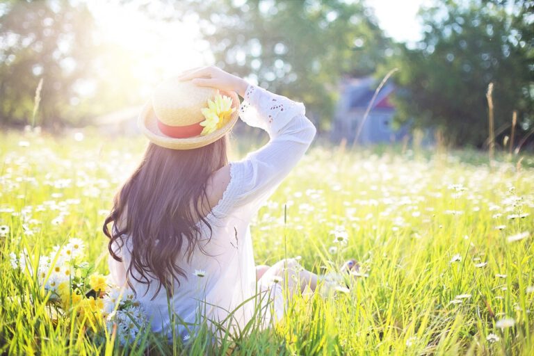 Eine Frau mit Hut sitzt an einem sonnigen Tag in einer Blumenwiese und genießt die Natur um sich herum.