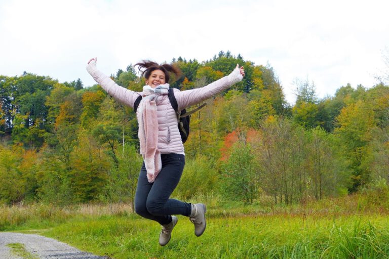 Eine Frau ist in der Natur unterwegs und springt voller Energie und Lebensfreude in die Luft.