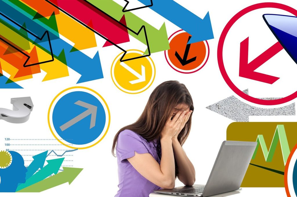 Eine Frau sitzt vor ihrem Laptop und hat vor Überforderung die Hände vors Gesicht geschlagen. Um sie herum sieht man viele bunte Pfeife, die in ihre Richtung zeigen und für den Druck stehen, unter dem sie leidet.