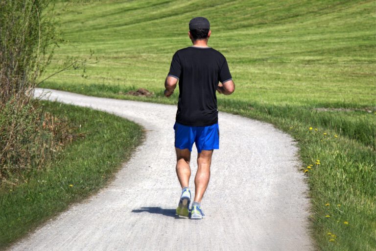 Ein Mann joggt auf einem Feldweg, umgeben von grünen Wiesen.