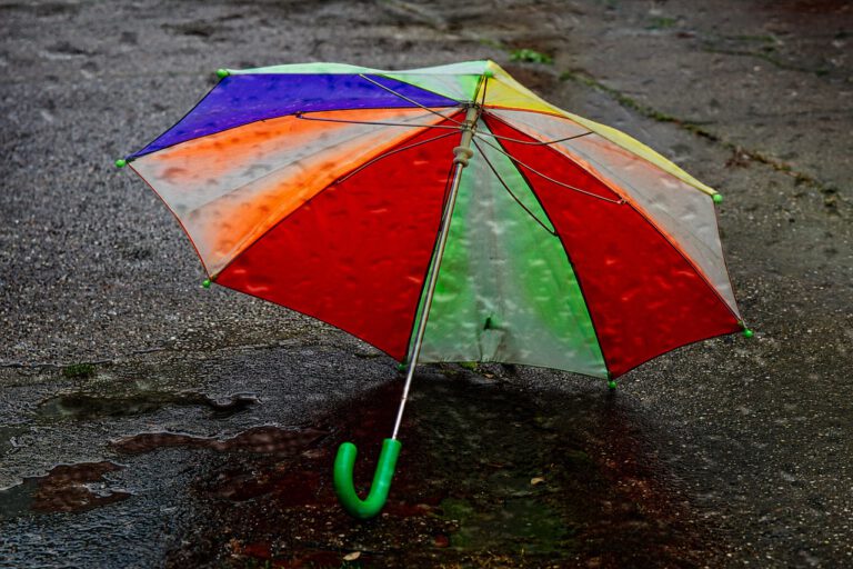 Auf einer nassen Straße steht ein bunter Regenschirm.