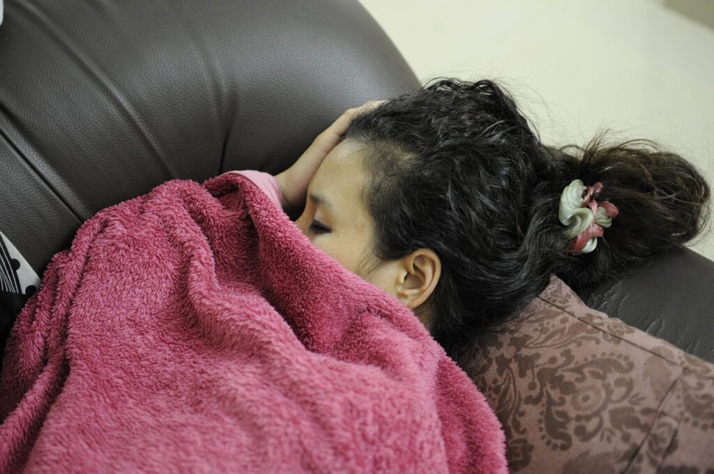 Eine erschöpfte Frau schläft zugedeckt mit einer roten Decke auf einer Couch