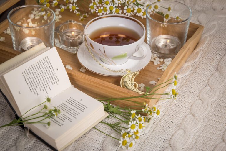Ein gemütliches Tablett mit einer Tasse Kamillentee, einem aufgeschlagenen Buch und drei brennenden Kerzen zur Entspannung.
